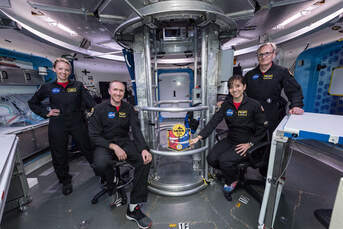 Will Daniels along with 3 other workers on the NASA project stand inside the capsule, facing the camera and smiling, all in their NASA uniforms.